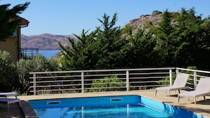 A swimming pool with a metal railing, two lounge chairs, and a view of the sea and mountains in the background. - Apartments Sunny (Karlobag)