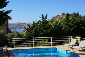 A swimming pool with a metal railing, two lounge chairs, and a view of the sea and mountains in the background. - Apartments Sunny (Karlobag)