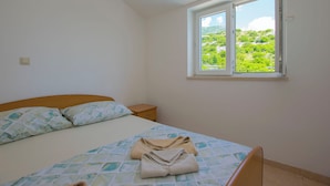 A bedroom with a bed, a nightstand, a window with a view of greenery, and a towel on the bed. - Apartments Sunny (Karlobag)