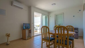 A dining area with a TV on a stand, a table with chairs, and a sofa. - Apartments Sunny (Karlobag)