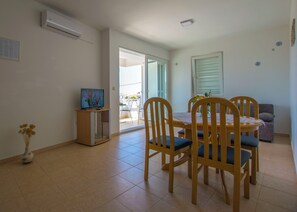 A dining area with a TV on a stand, a table with chairs, and a sofa. - Apartments Sunny (Karlobag)