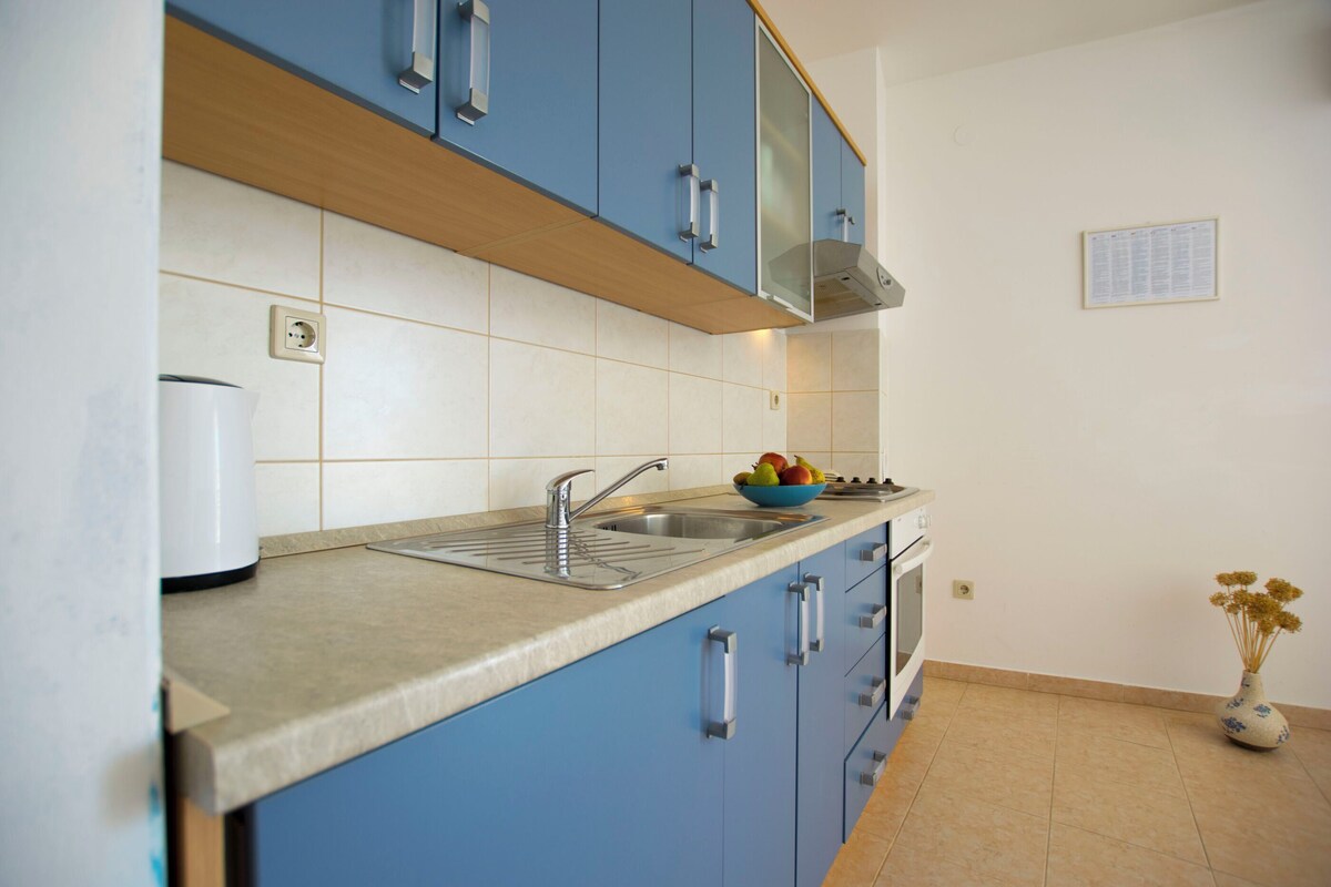A kitchen with blue cabinets, a stainless steel sink, and a white countertop.