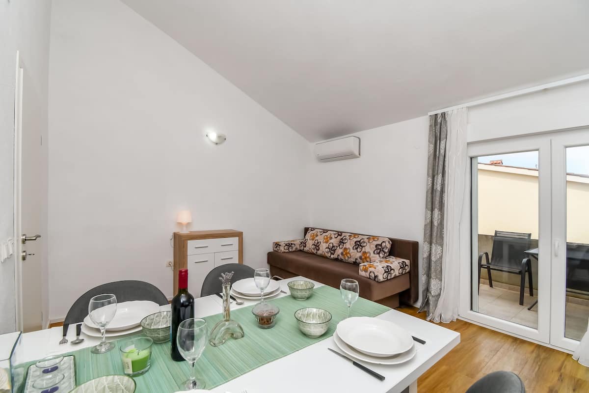 A dining area with a table set for four, a sofa, and a sliding glass door leading to an outdoor area.