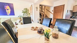 A dining area with a table set for two, featuring a vase with flowers, a jar, and bread. There is a staircase leading to another room, and a television mounted on the wall. - Apartment Bilice (Bilice)