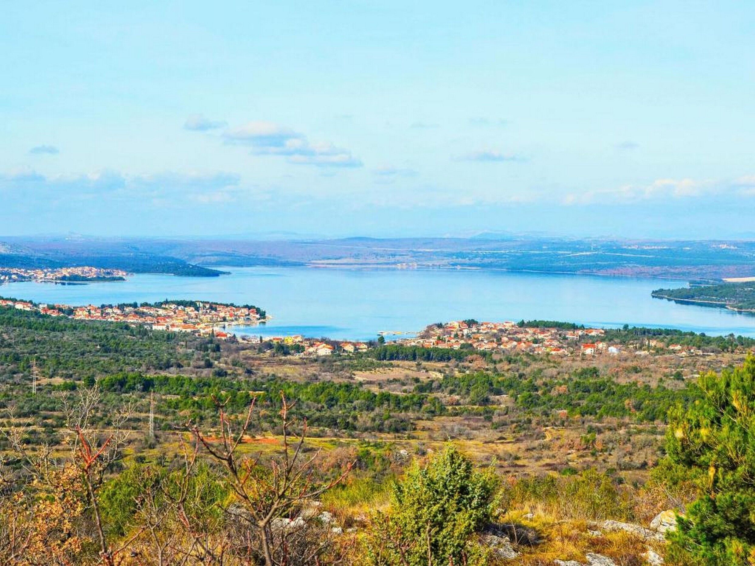 A coastal landscape with a view of a town by the sea, surrounded by hills and greenery.