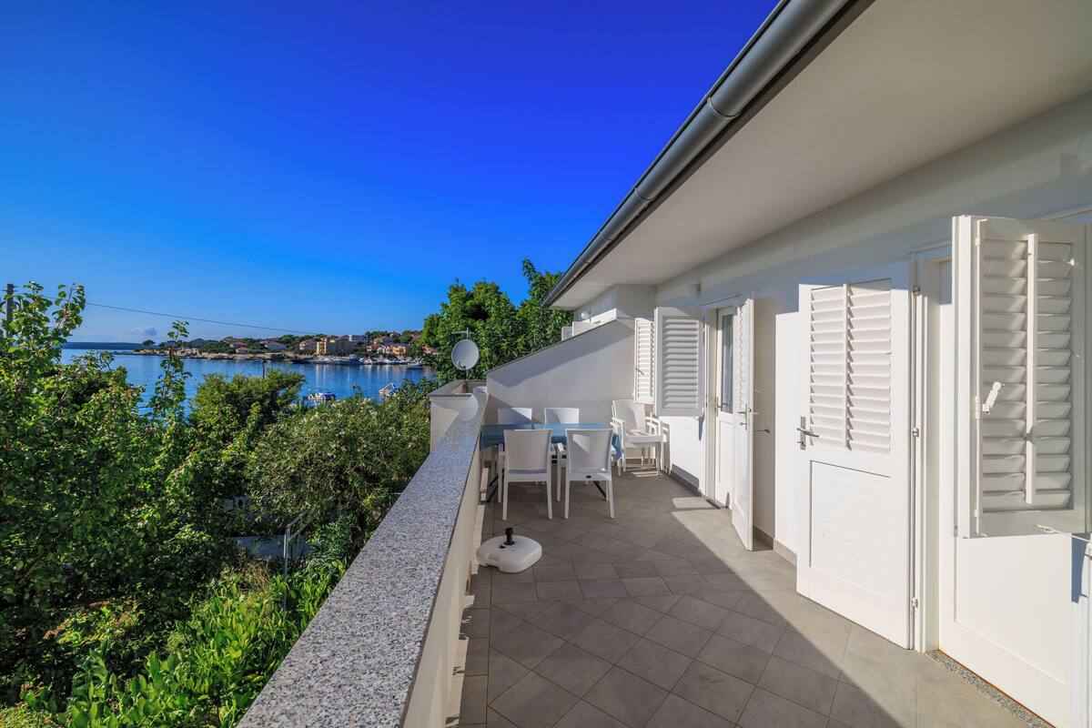 Un balcon avec vue sur la mer, des volets blancs et une table avec des chaises.