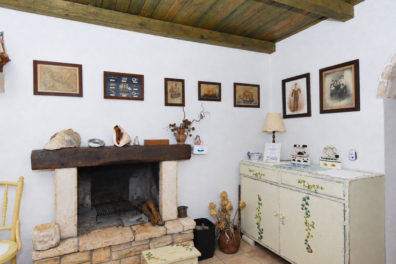 A cozy room with a stone fireplace, wooden mantel, and a white cabinet with decorative items.
