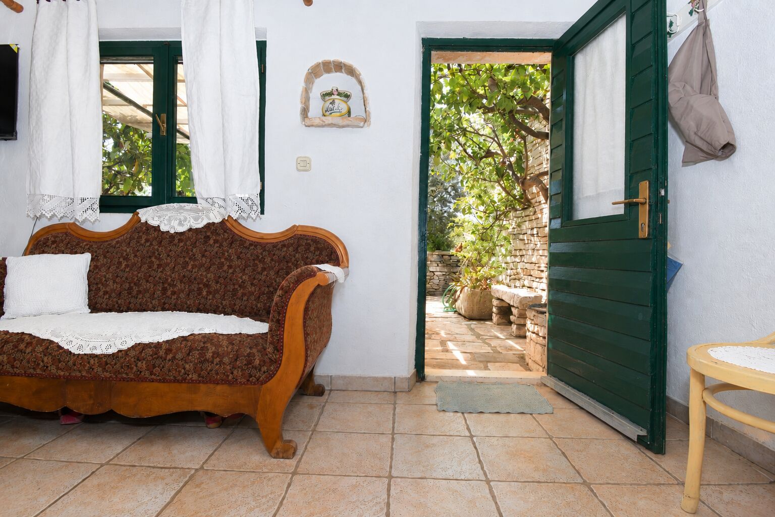 A cozy room with a wooden sofa, a small table, and a green door leading to an outdoor area with a stone wall and plants.