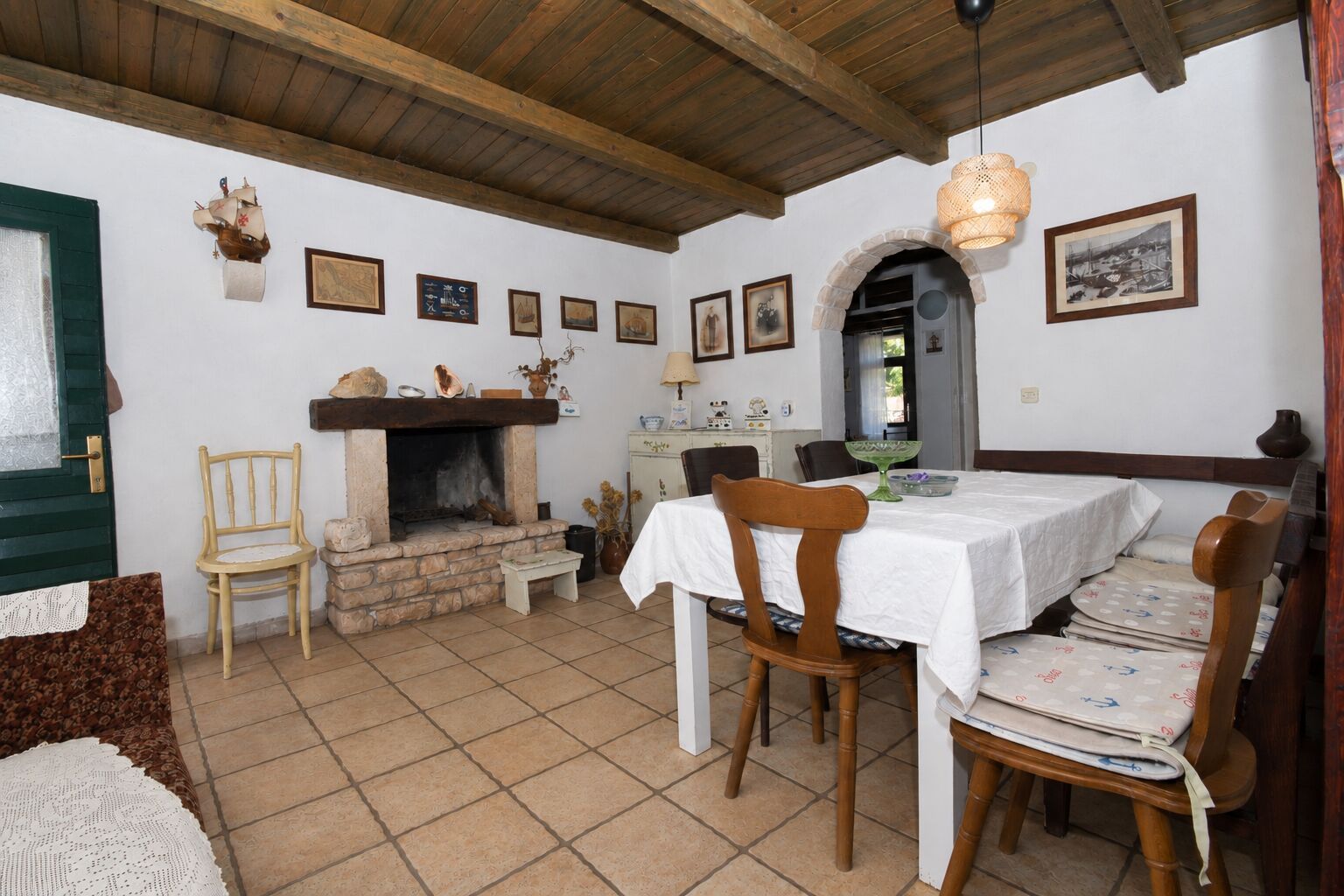 A rustic dining area with a fireplace, wooden chairs, a table set for four, and a tiled floor.
