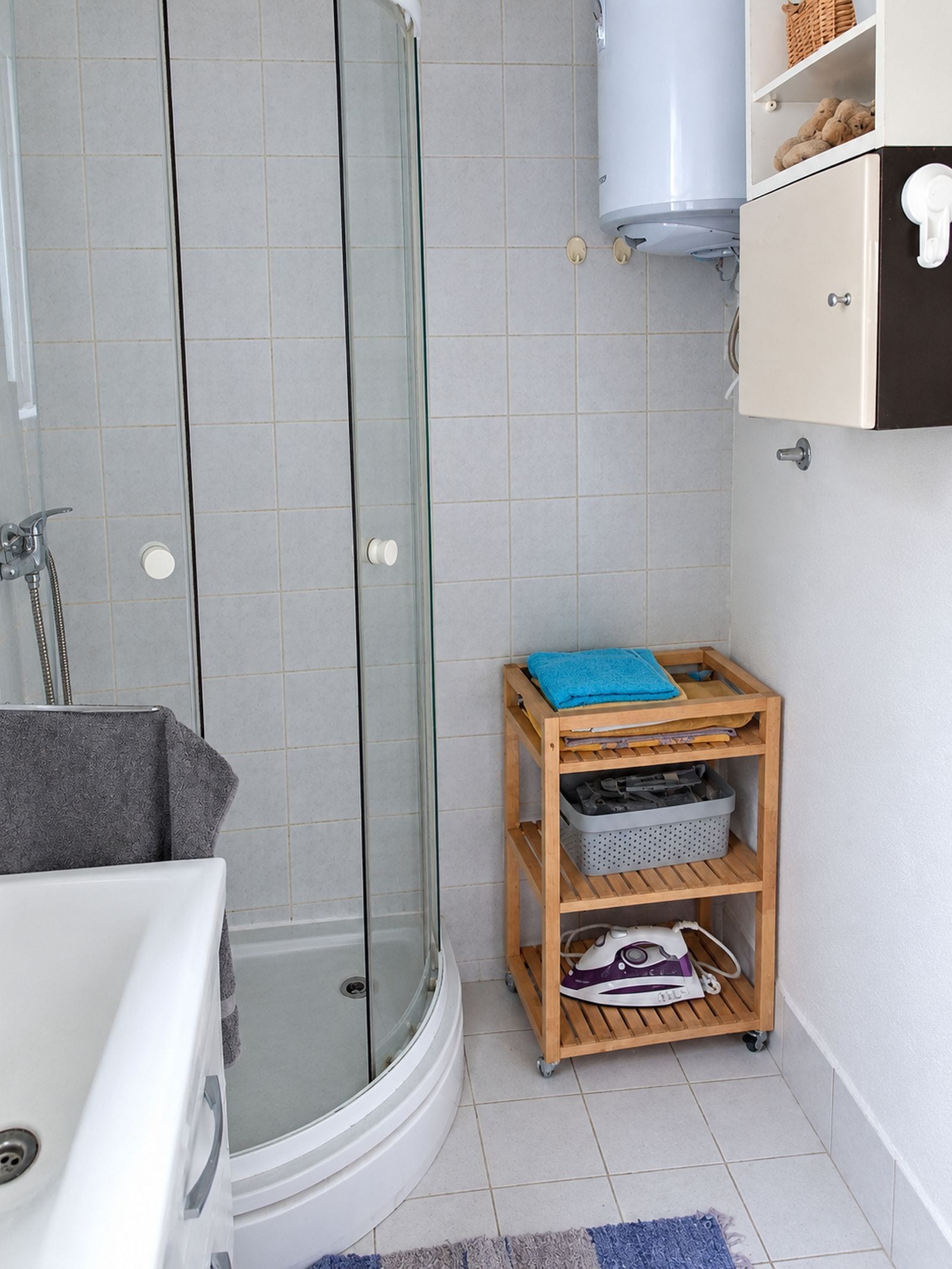 Une salle de bain avec une douche à parois de verre, une étagère en bois avec des serviettes et une baignoire blanche.