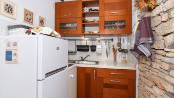 Una cocina compacta con armarios de madera, un refrigerador blanco y una pared de piedra.