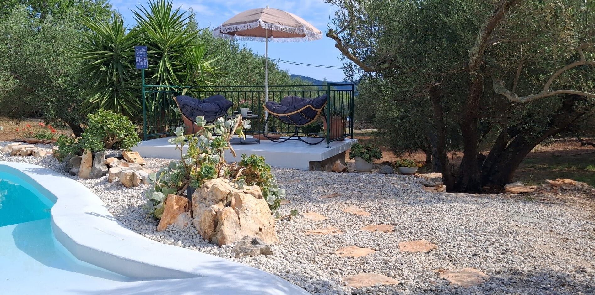 A pool area with a lounge chair and umbrella, surrounded by rocks and plants.