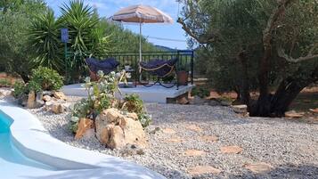 Un área de piscina con una tumbona y sombrilla, rodeada de rocas y plantas.
