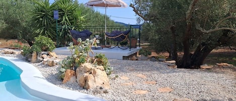 A pool area with a lounge chair and umbrella, surrounded by rocks and plants.