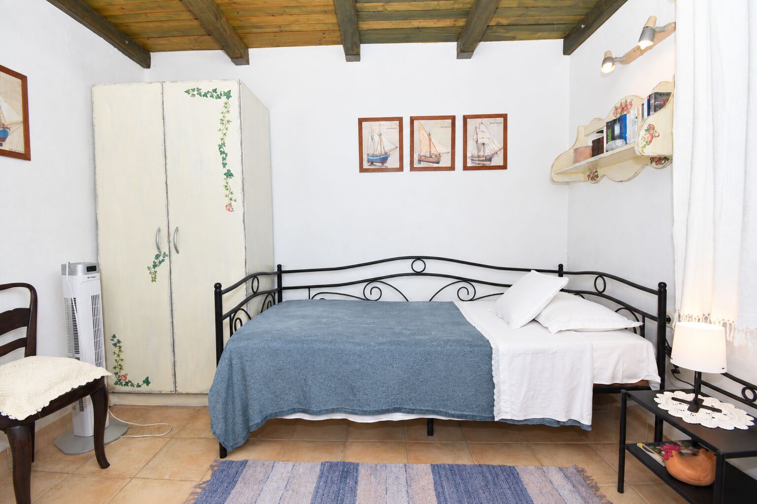 Un dormitorio con una cama, un armario, una silla y una estantería con libros.