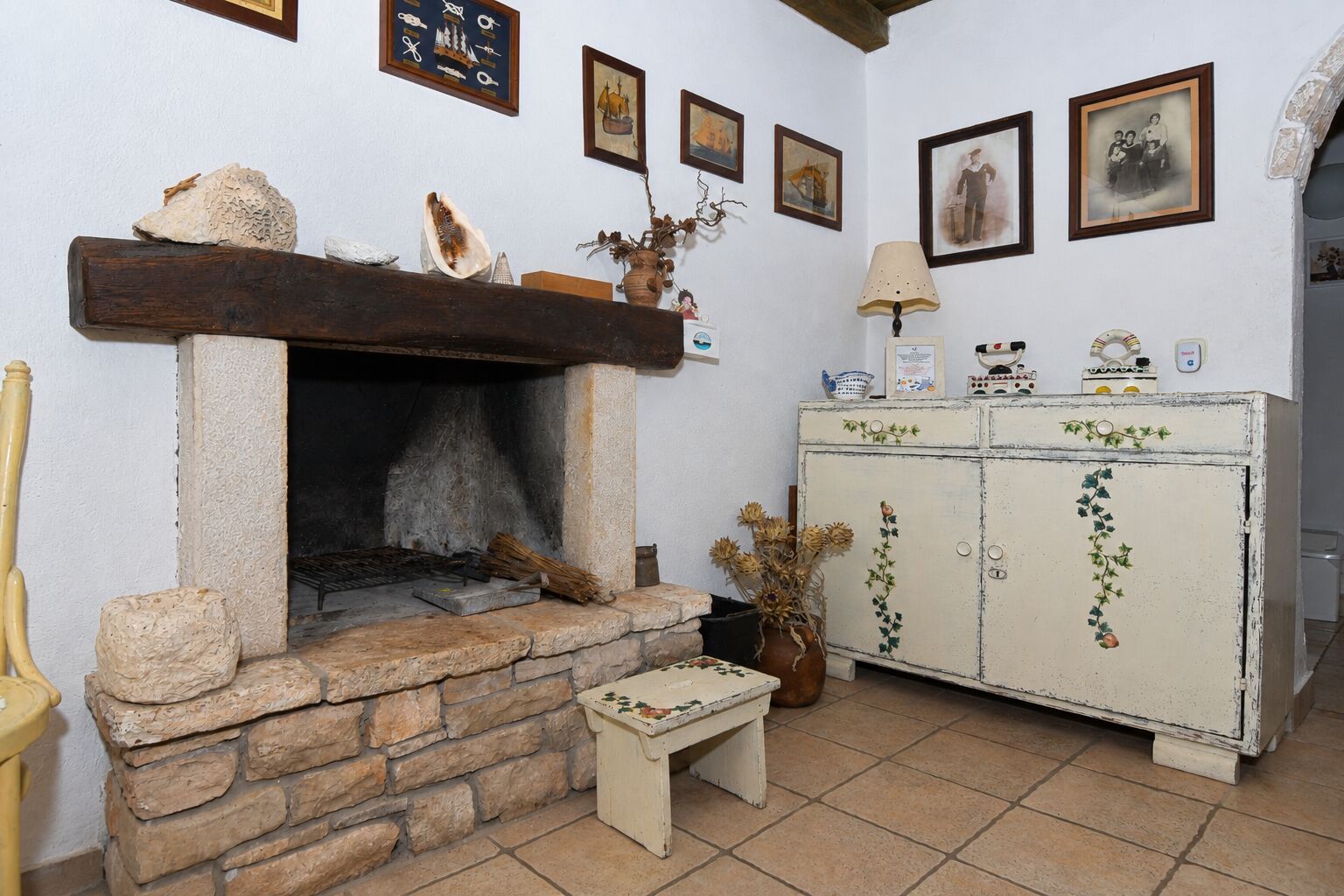 Una habitación rústica con chimenea de piedra, un banco de madera y un aparador antiguo decorado con hiedra.
