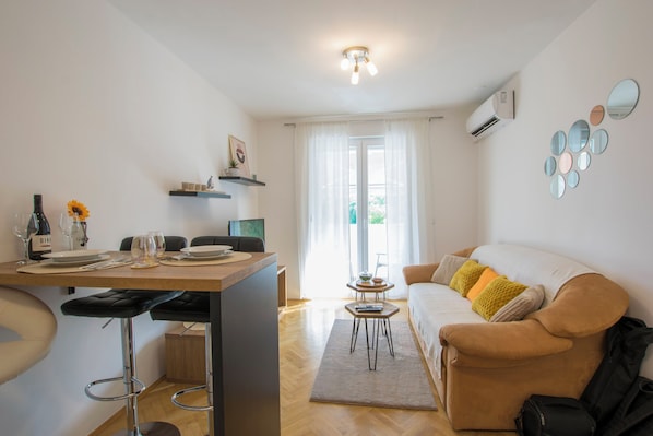 A modern living room with a sofa, a coffee table, and a dining area with a table set for two. - Apartment Molly (Rijeka)