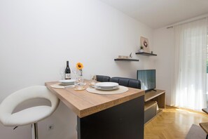 A dining area with a wooden table, white chair, and a TV on a stand. - Apartment Molly (Rijeka)