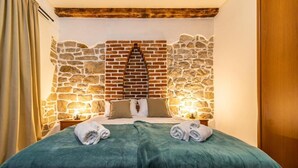 A cozy room with a stone wall, a bed with green bedding, and two bedside lamps. - House Garden House (Rab)