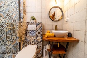 Een badkamer met toilet, wastafel en douche. Boven de wastafel hangt een spiegel en er is een wandlamp.