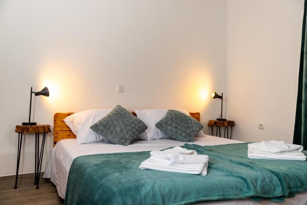 Un lit bien fait, avec une couverture verte et des oreillers, deux lampes de chevet et une pile de serviettes pliées posée sur le lit.