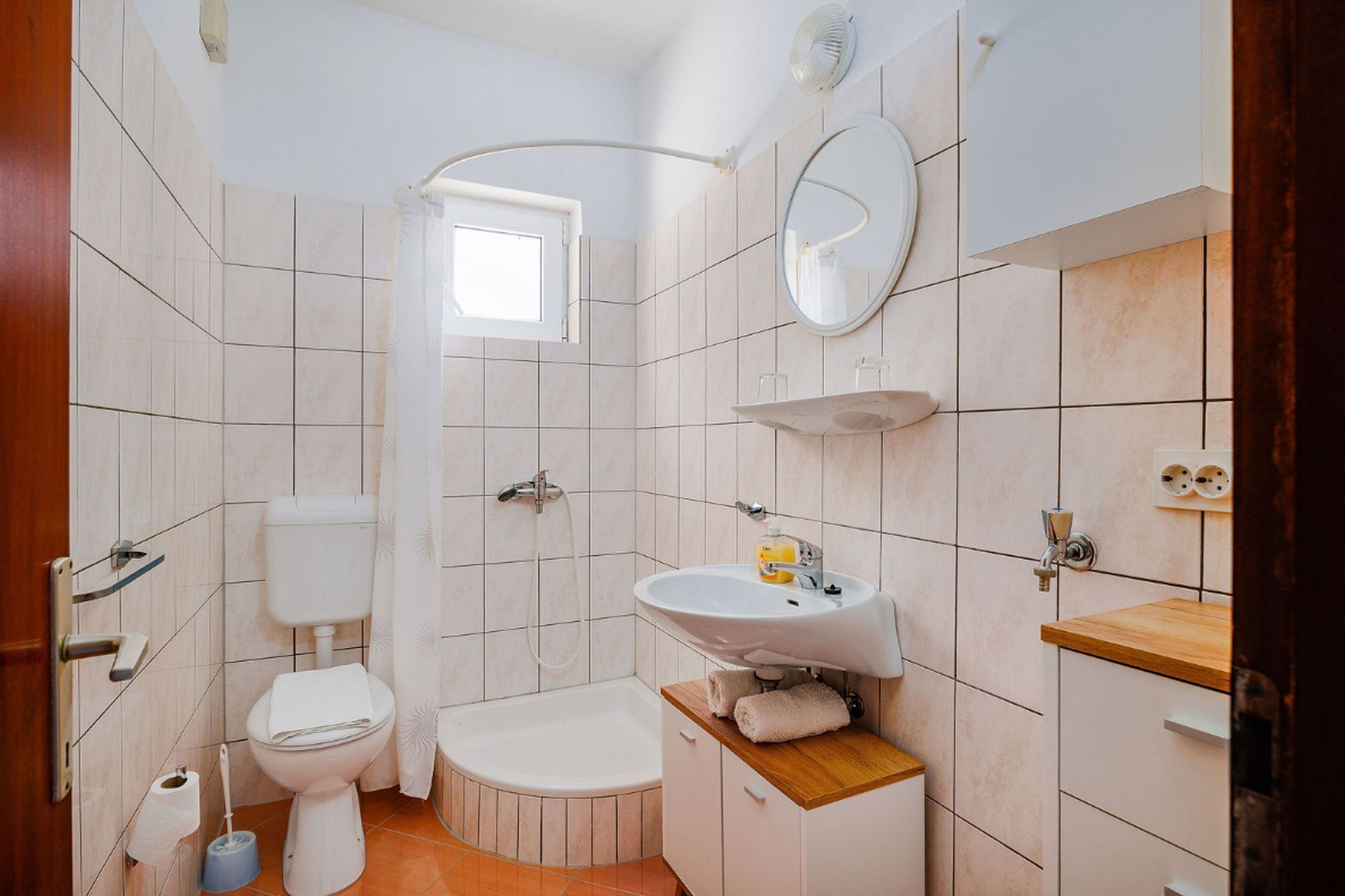 A bathroom with a toilet, bidet, sink, mirror, and a small window.