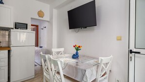 Une cuisine compacte équipée d’un four à micro-ondes, d’un four et d’une petite table avec des chaises. Un téléviseur à écran plat est fixé au mur au-dessus de la table.