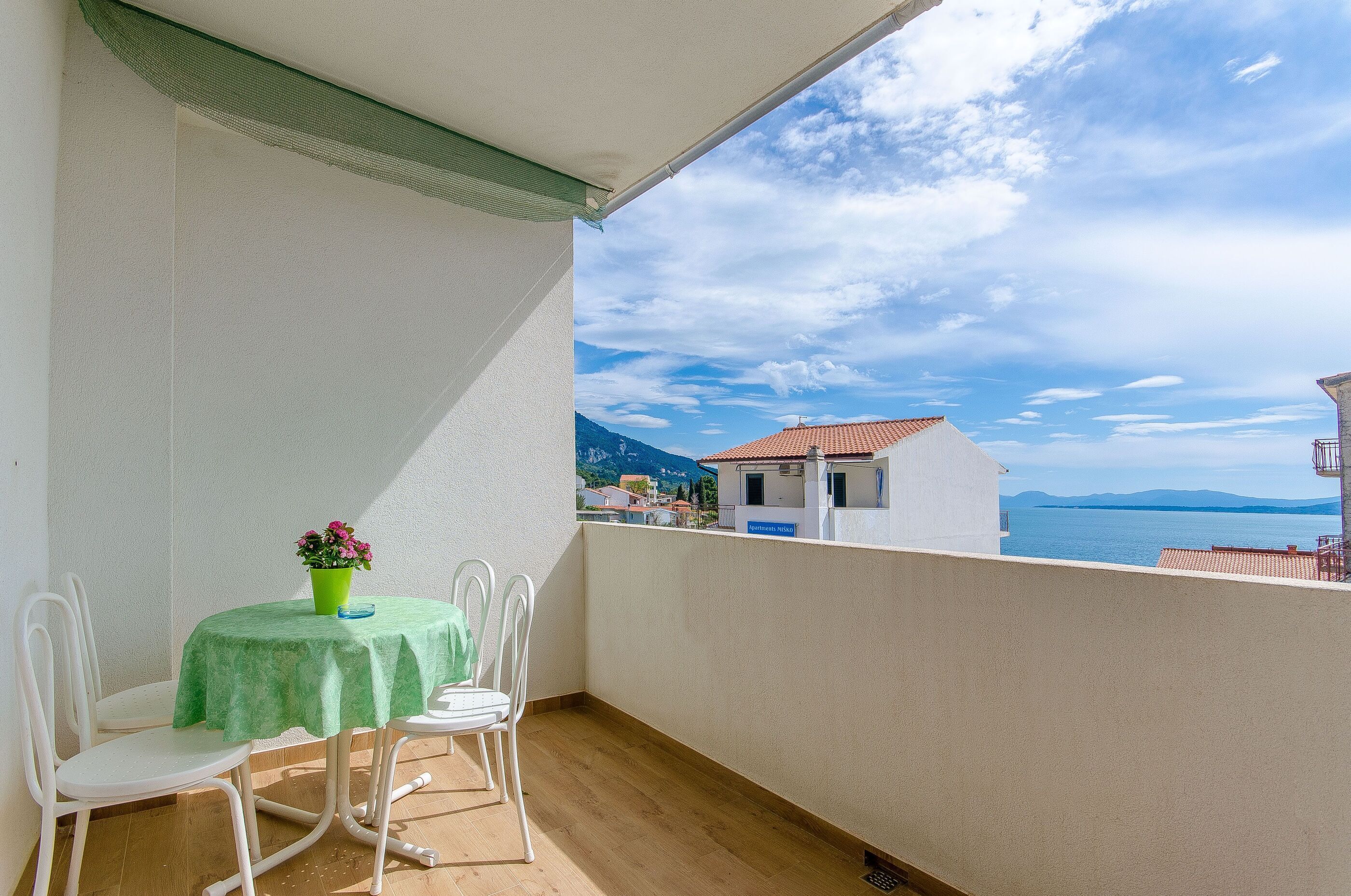 A balcony with a table and chairs, a green tablecloth, and a potted plant.