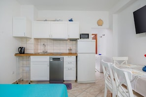 Une cuisine compacte avec des meubles blancs, un four à micro-ondes, un réfrigérateur, un évier et un coin repas comprenant une table et des chaises.
