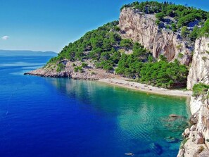 Un paisaje costero con un acantilado rocoso, aguas turquesas cristalinas y una playa arenosa.