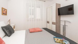 Un dormitorio moderno con cama, televisor de pantalla plana, armario y ventana con cortinas translúcidas.