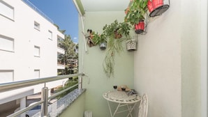 Un balcón con baranda de metal blanco, una mesa pequeña con una silla y varias plantas en macetas.