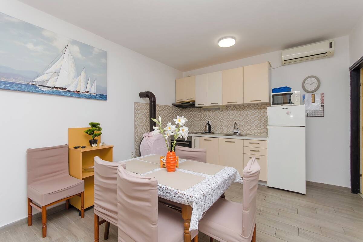 Un coin repas avec une table dressée pour quatre personnes, un vase rempli de fleurs et un tableau représentant des voiliers accroché au mur.