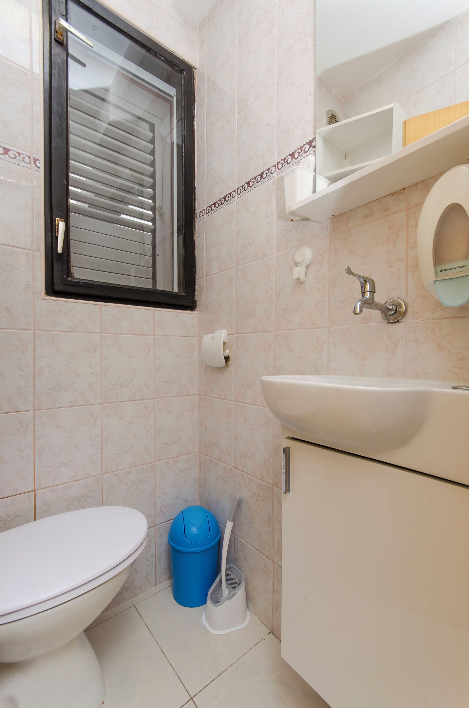 A bathroom with a toilet, sink, and window with blinds.