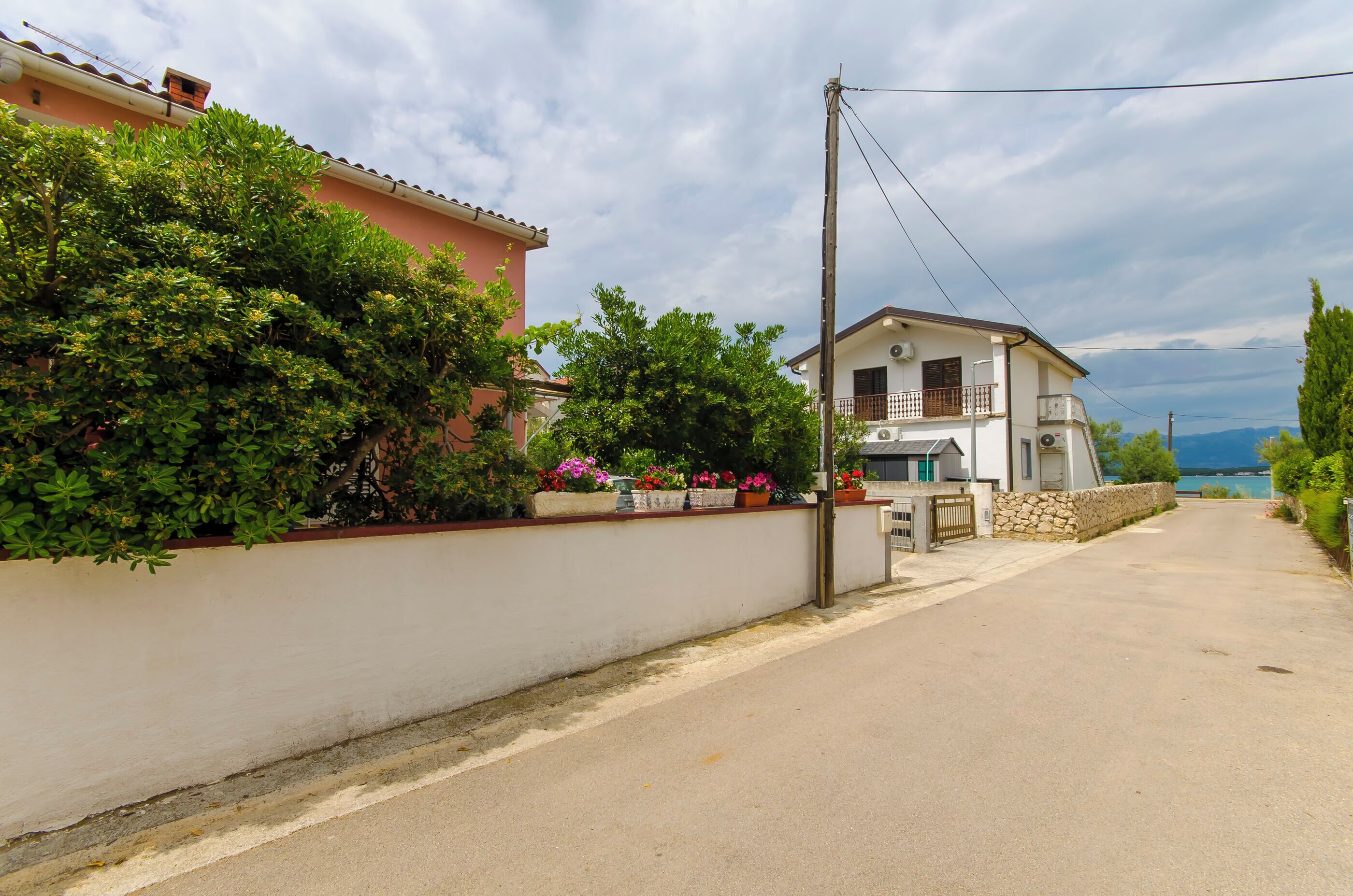 Une rue résidentielle bordée de maisons, un mur blanc orné de plantes en pot et un ciel dégagé.