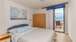 Quarto com cama, guarda-roupa, pintura de veleiros e vista para o mar através de uma porta de correr.