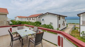 Terraço com mesa e cadeiras, com vista para uma área residencial com casas e o mar.