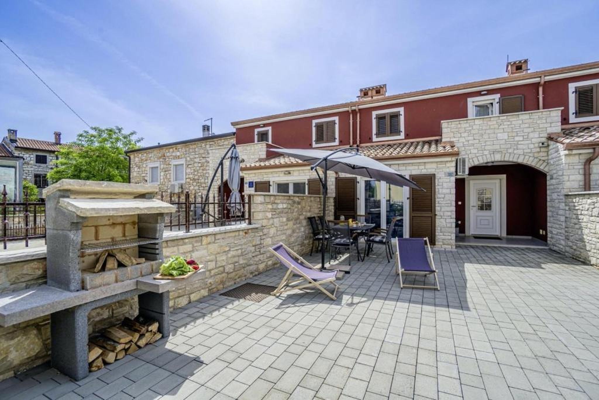 Un patio con una parrilla de piedra, sillas de descanso y un comedor con sombrillas.