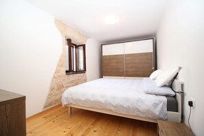 Une chambre à coucher avec un lit, un plancher en bois, un mur en pierre, une fenêtre et une table de chevet.