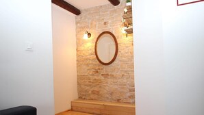 Una habitación con pared de piedra, un banco de madera y un espejo redondo.