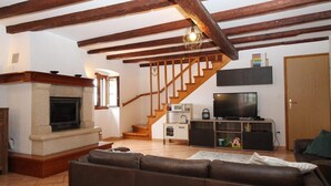 Una sala de estar con chimenea, un sofá, una televisión y una zona de cocina con una escalera.