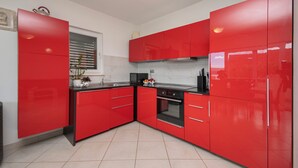 A modern kitchen with red cabinetry, a stainless steel sink, and a built-in oven. - House Mimica (Omis)