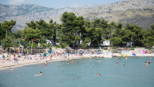 A beach with people sunbathing and swimming, surrounded by trees and buildings. - Apartments Family Spacious (Split)