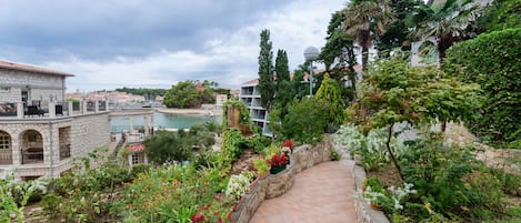 A garden pathway leading to a stone building with a view of a body of water and surrounding greenery.