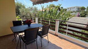 Un balcon avec une table et des chaises, un espace abrité et une vue sur une maison et des arbres.