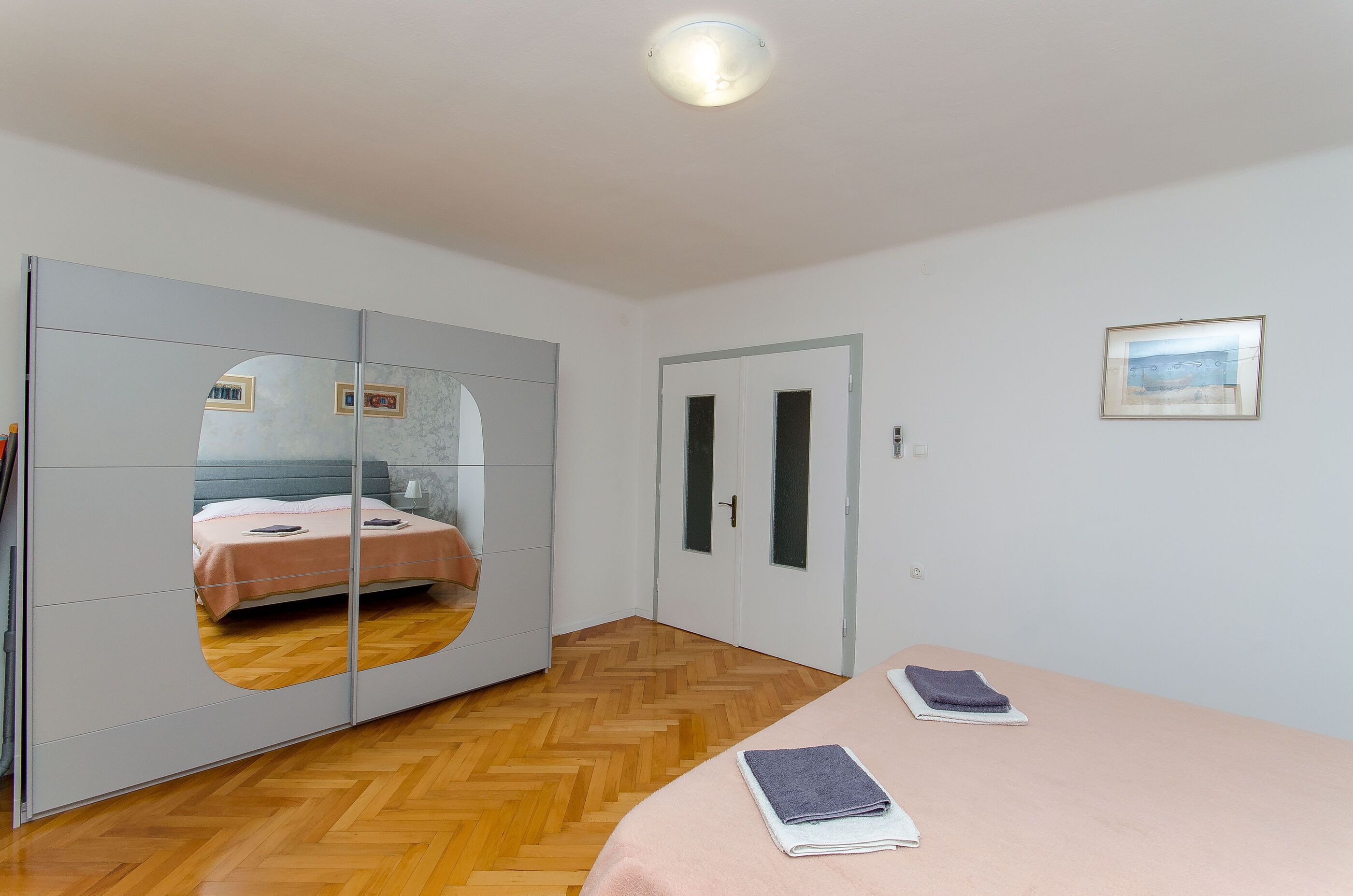 A bedroom with a bed, a wardrobe with a mirror, a door, and a framed picture on the wall.