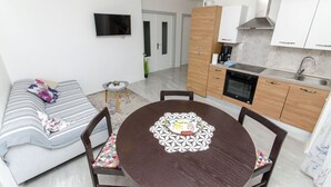 A compact living space with a sofa, a dining table with chairs, a kitchenette, and a TV mounted on the wall. - Apartment Sun City (Split)