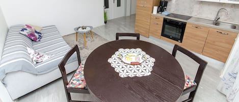A compact living space with a sofa, a dining table with chairs, a kitchenette, and a TV mounted on the wall.