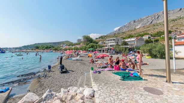 Une plage où l’on voit des gens se prélasser au soleil, nager et des bateaux sur l’eau.