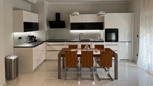 Une cuisine moderne avec des armoires blanches, un comptoir noir et une table à manger avec quatre chaises. Des luminaires suspendus sont placés au-dessus du comptoir, et une poubelle se trouve à gauche.